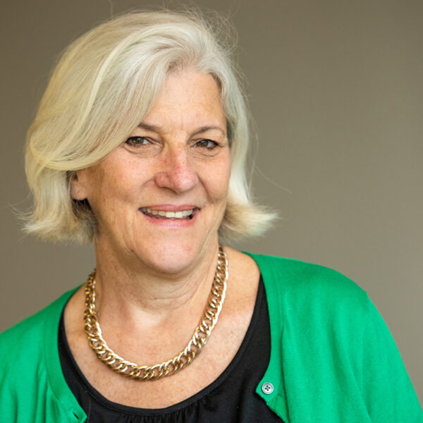 Portrait of Anna Young smiling in a black top, green cardigan, and thick gold chain necklace.