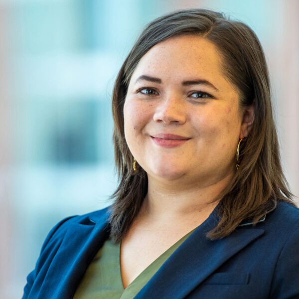 Portrait of Bailey Shea smiling in a navy blue blazer, green top, and gold hoop earrings.