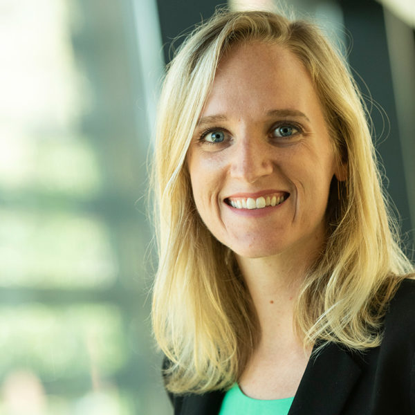 Portrait of Emily Wyche smiling in a black blazer in front of a window.