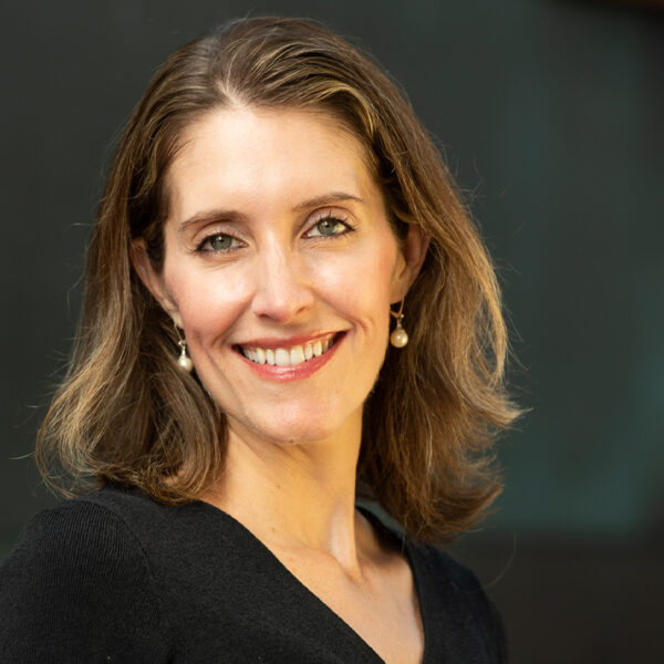 Portrait of Leslie Murphy smiling in a black top with pearl drop earrings.