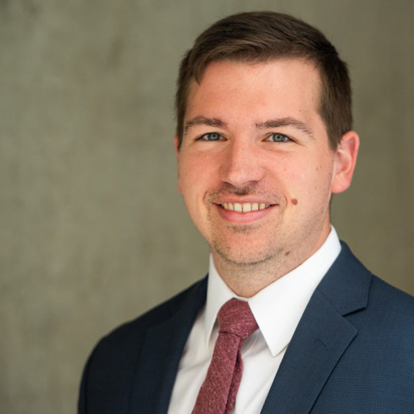 Portrait of Nick Guidi smiling in a suit and red tie.