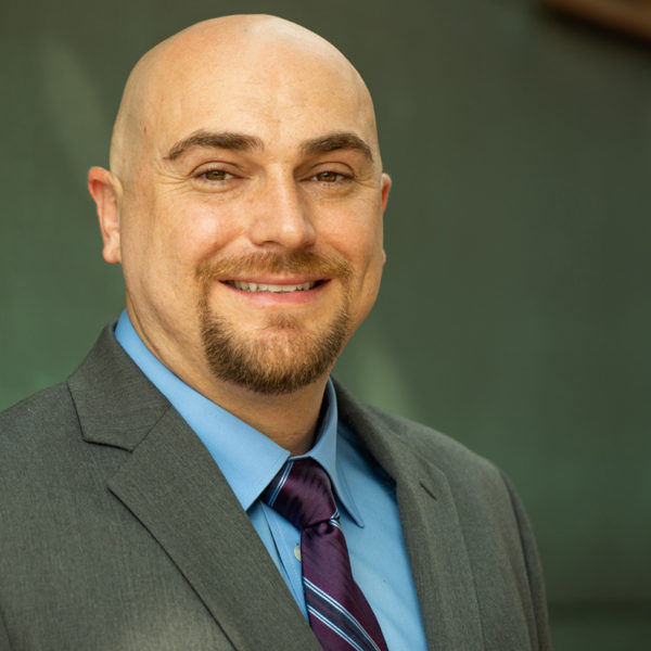 Portait of Travis Marrs smiling in a suit and purple tie.